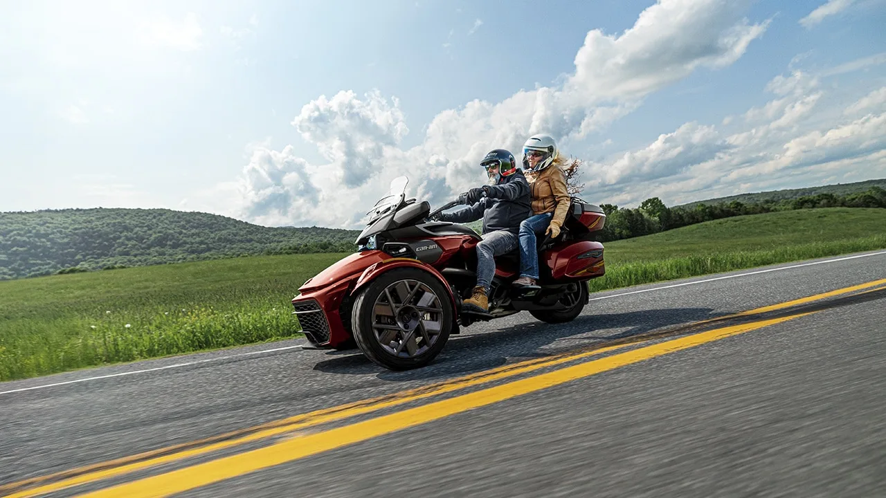 骑手驾驶红色庞巴迪 Can-Am Spyder F3 倒三轮载着乘客行驶在乡间公路上